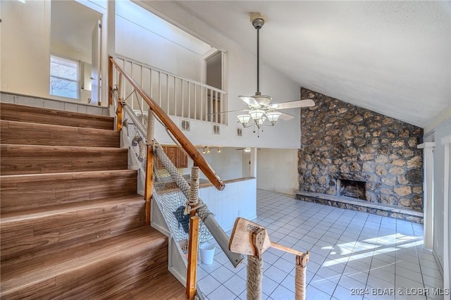 staircase featuring tile patterned flooring, high vaulted ceiling, ceiling fan, and a stone fireplace