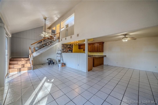 unfurnished living room with wooden walls, ceiling fan, lofted ceiling, and light tile patterned floors