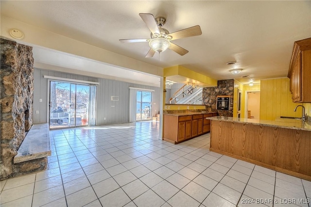 kitchen with sink, ceiling fan, light tile patterned floors, black oven, and kitchen peninsula