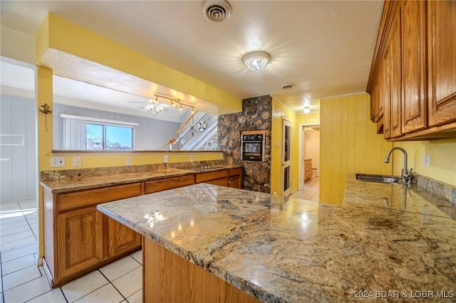 kitchen with kitchen peninsula, light stone countertops, ceiling fan, sink, and black oven