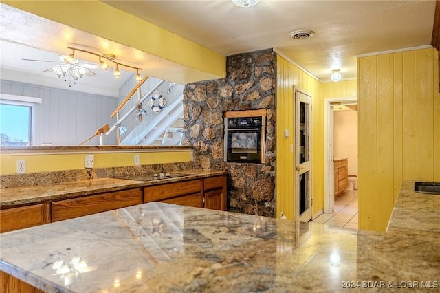 kitchen featuring ornamental molding, ceiling fan, wooden walls, black appliances, and light tile patterned floors