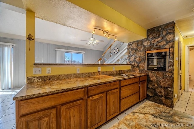 kitchen featuring kitchen peninsula, ceiling fan, black appliances, stone counters, and light tile patterned flooring