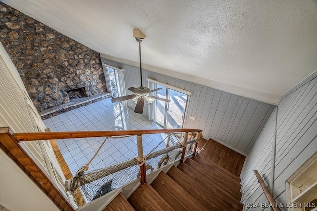 staircase with hardwood / wood-style floors, ceiling fan, wood walls, and lofted ceiling