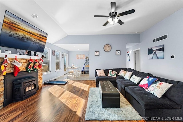 living room featuring vaulted ceiling, hardwood / wood-style flooring, a wood stove, and ceiling fan