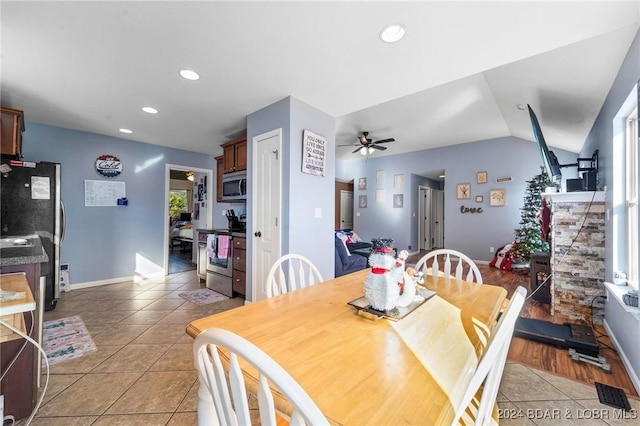 dining room featuring ceiling fan, a fireplace, vaulted ceiling, and light wood-type flooring