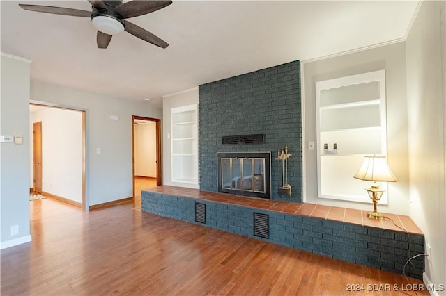 unfurnished living room with ornamental molding, ceiling fan, hardwood / wood-style flooring, built in features, and a fireplace