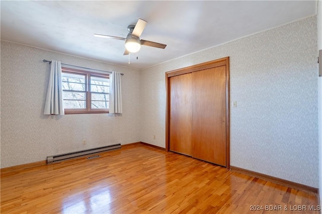 unfurnished bedroom featuring a baseboard heating unit, ceiling fan, ornamental molding, light hardwood / wood-style floors, and a closet