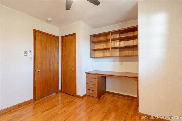 unfurnished office featuring built in desk, light hardwood / wood-style flooring, ceiling fan, and crown molding