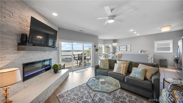 living room with a stone fireplace, hardwood / wood-style floors, and ceiling fan with notable chandelier