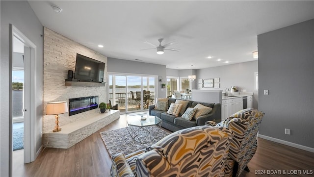 living room with hardwood / wood-style flooring, a stone fireplace, ceiling fan, and sink