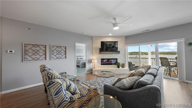 living room featuring hardwood / wood-style floors, ceiling fan, and a stone fireplace