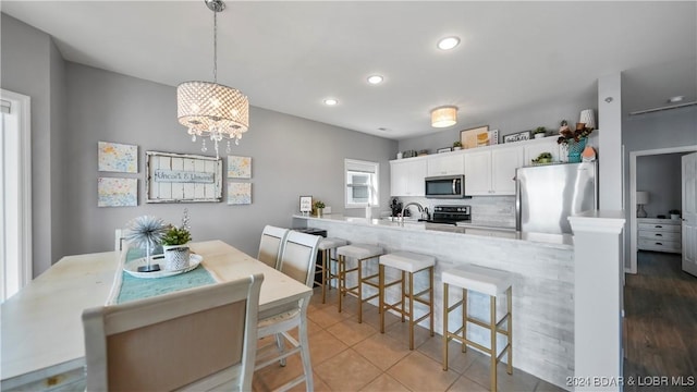 kitchen featuring kitchen peninsula, a kitchen bar, stainless steel appliances, white cabinetry, and hanging light fixtures