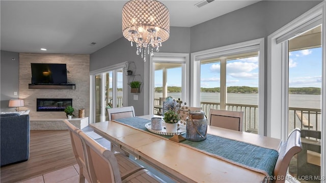 dining space with a large fireplace, a water view, a notable chandelier, and light hardwood / wood-style flooring