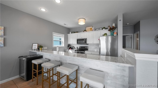 kitchen featuring a kitchen bar, white cabinetry, kitchen peninsula, and appliances with stainless steel finishes