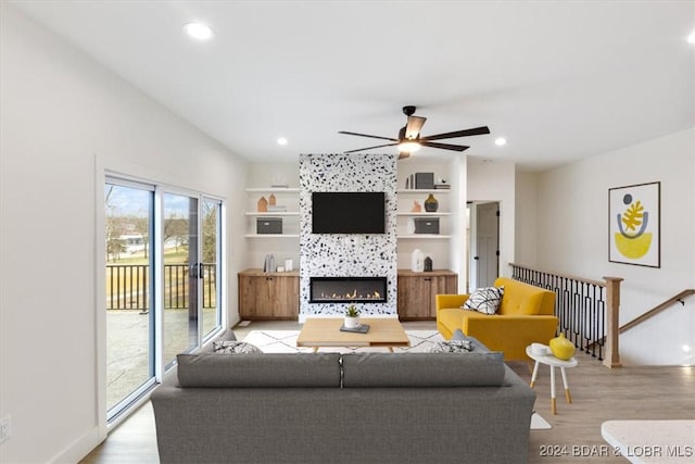 living room with a tile fireplace, ceiling fan, built in shelves, and light wood-type flooring