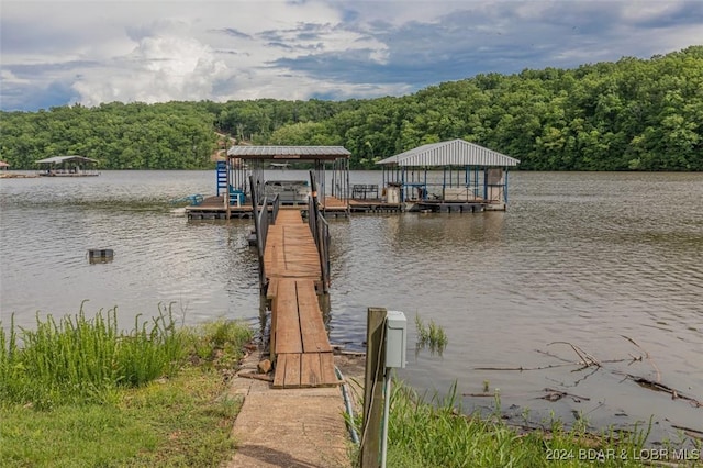 view of dock featuring boat lift, a water view, and a wooded view