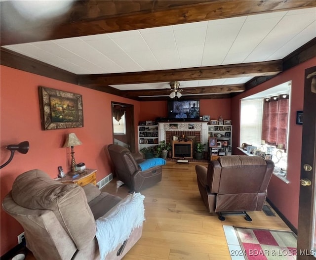 living room with a fireplace, light wood finished floors, visible vents, beamed ceiling, and baseboards