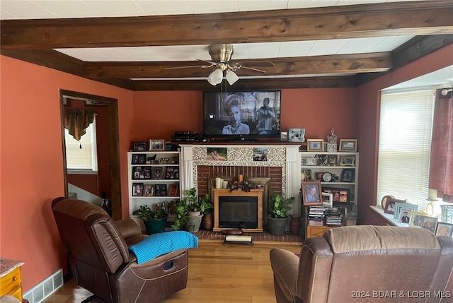 living room with visible vents, a ceiling fan, wood finished floors, a brick fireplace, and beam ceiling