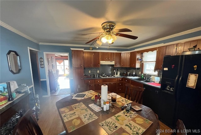 kitchen featuring crown molding, tasteful backsplash, a sink, under cabinet range hood, and black appliances