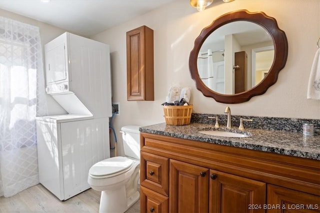 bathroom featuring wood-type flooring, vanity, toilet, and stacked washer / dryer