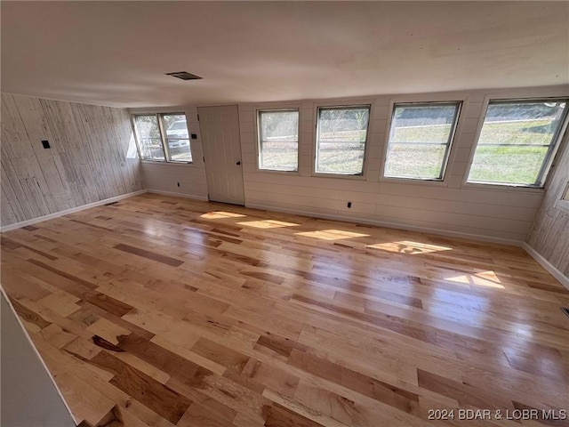 empty room featuring wooden walls, light hardwood / wood-style floors, and a healthy amount of sunlight