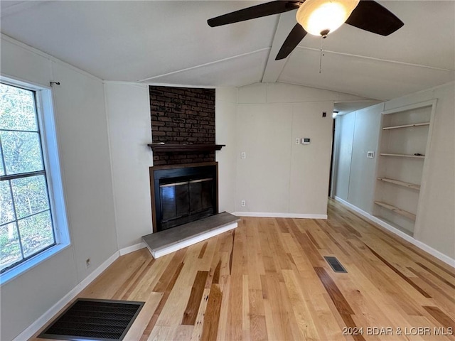 unfurnished living room with a wealth of natural light, a fireplace, lofted ceiling with beams, and light wood-type flooring