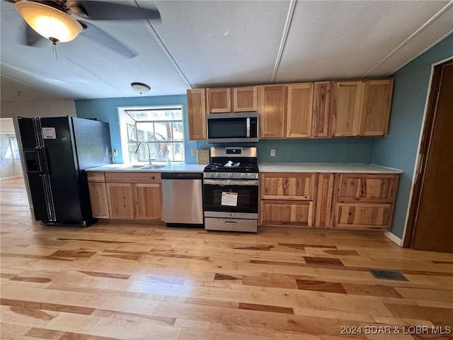 kitchen with a textured ceiling, light hardwood / wood-style flooring, vaulted ceiling, and appliances with stainless steel finishes