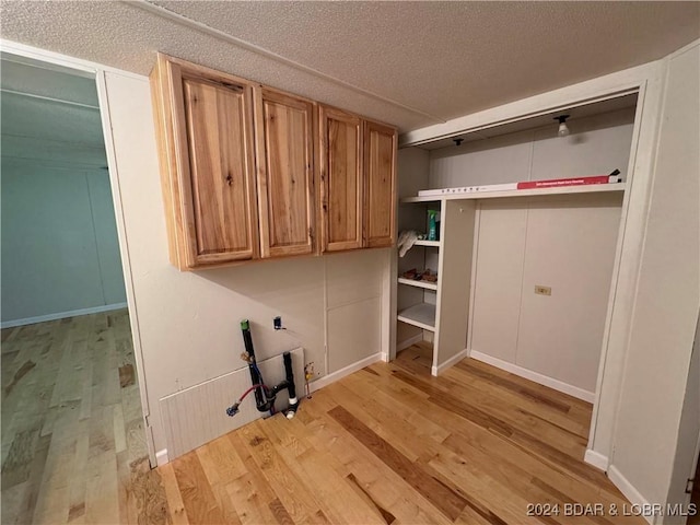 clothes washing area featuring cabinets, a textured ceiling, and light wood-type flooring