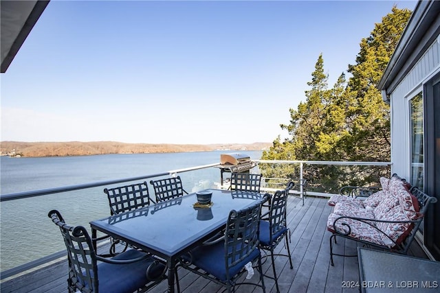 wooden terrace featuring a grill, a water view, and outdoor dining space
