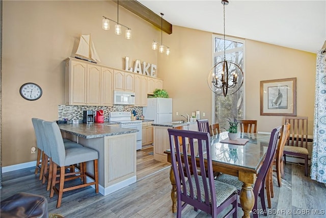 dining space with baseboards, light wood finished floors, high vaulted ceiling, and a notable chandelier