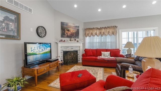 living room with hardwood / wood-style floors, a stone fireplace, and lofted ceiling