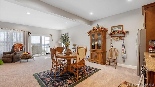 dining space featuring beamed ceiling and light colored carpet