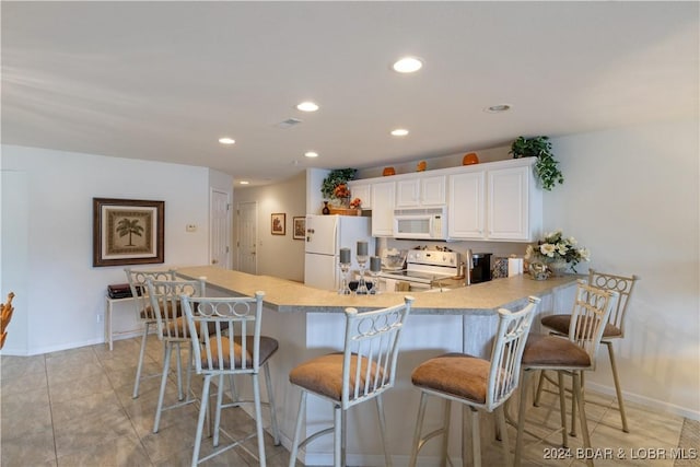 kitchen featuring white appliances, white cabinets, a kitchen breakfast bar, light tile patterned floors, and kitchen peninsula