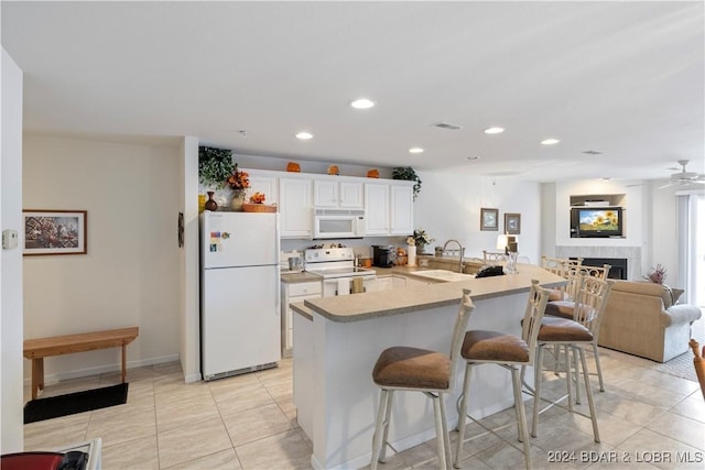 kitchen with kitchen peninsula, white appliances, a kitchen bar, a fireplace, and white cabinets