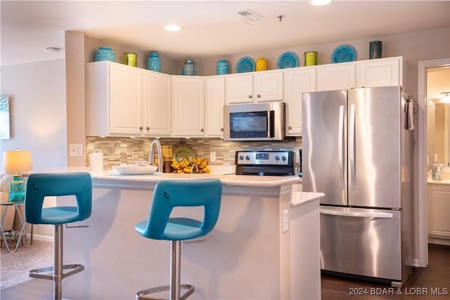 kitchen featuring a kitchen breakfast bar, kitchen peninsula, appliances with stainless steel finishes, tasteful backsplash, and white cabinetry