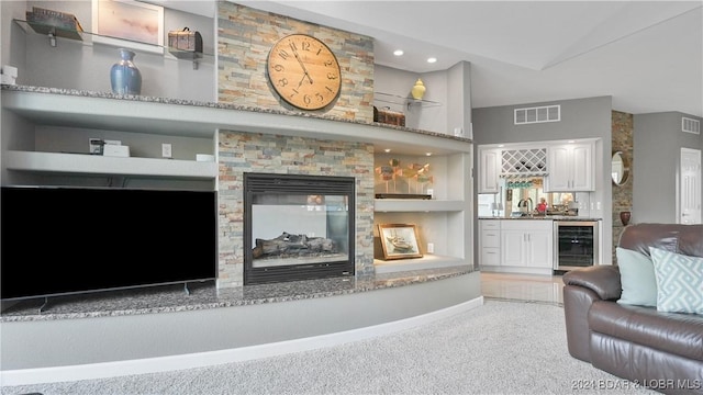 carpeted living room with built in shelves, indoor wet bar, a fireplace, and wine cooler