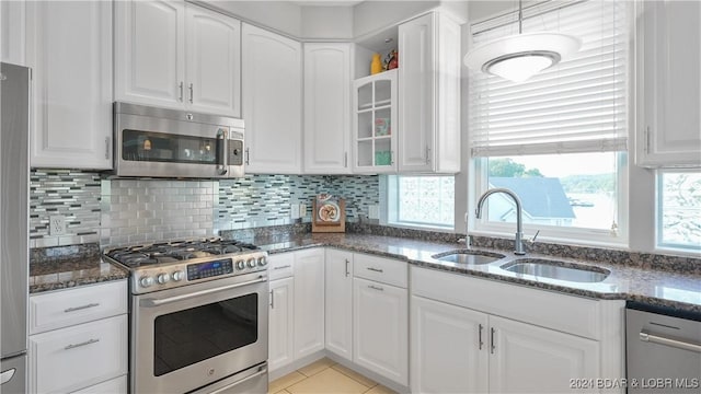 kitchen with white cabinets, sink, dark stone countertops, appliances with stainless steel finishes, and light tile patterned flooring