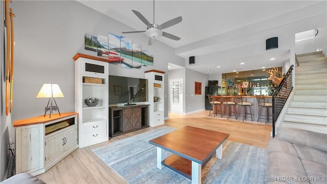 living room with ceiling fan, light hardwood / wood-style floors, a towering ceiling, and indoor bar