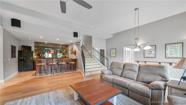 living room featuring ceiling fan with notable chandelier, light hardwood / wood-style floors, and indoor bar