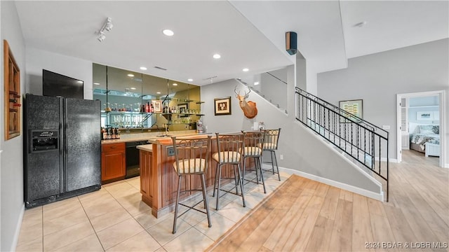 kitchen with kitchen peninsula, light wood-type flooring, a breakfast bar area, and black appliances