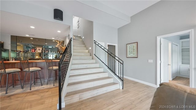 staircase with bar area, wood-type flooring, and a high ceiling