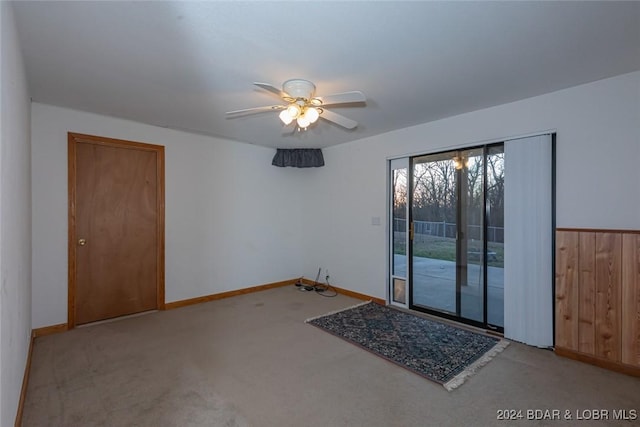 spare room with ceiling fan, wooden walls, and light colored carpet