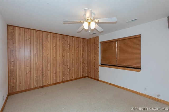 spare room with ceiling fan, wood walls, and light carpet