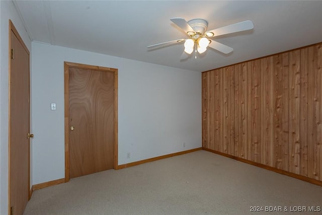 empty room featuring wooden walls, ceiling fan, and light colored carpet