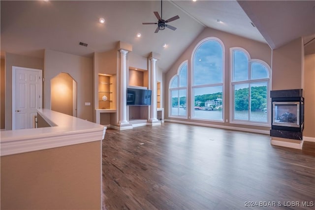 825 Grand View Dr, Porto Cima, MO 65079 - unfurnished living room featuring a multi sided fireplace, ornate columns, built in shelves, dark wood-style floors, and high vaulted ceiling