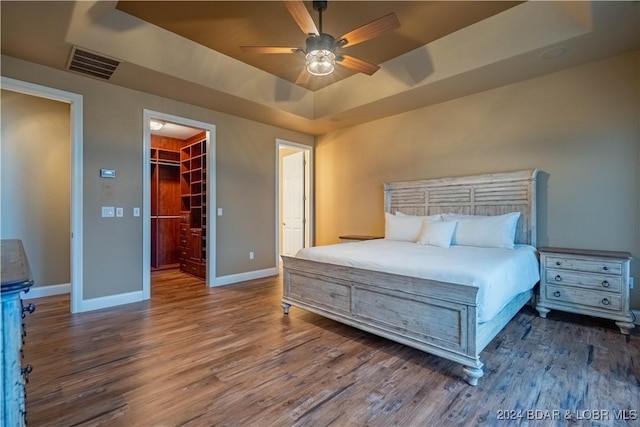 bedroom with hardwood / wood-style floors, a walk in closet, a tray ceiling, and ceiling fan