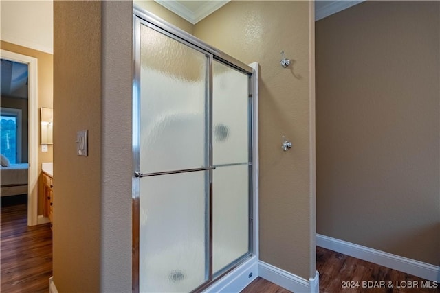 bathroom with wood-type flooring, a shower with shower door, and ornamental molding