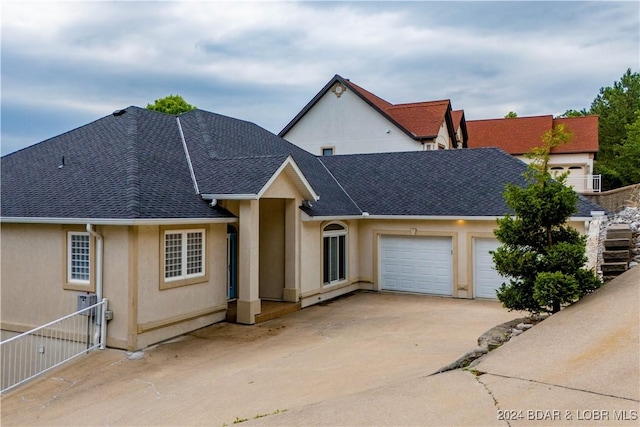 825 Grand View Dr, Porto Cima, MO 65079 - view of front of property featuring a shingled roof, concrete driveway, an attached garage, and stucco siding