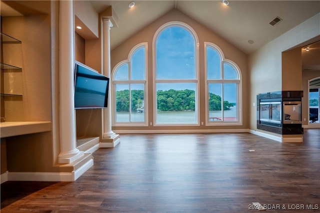 unfurnished living room with a multi sided fireplace, dark wood-type flooring, high vaulted ceiling, and decorative columns