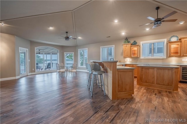 kitchen featuring ceiling fan, dark wood-type flooring, wine cooler, a kitchen bar, and a kitchen island